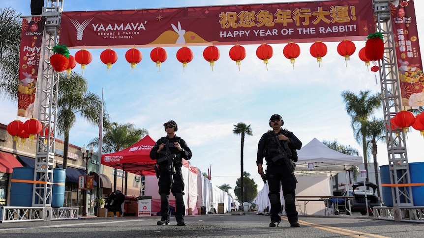 Armed police stand under a Chinese new year banner and lanterns on a street. 