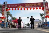 Armed police stand under a Chinese new year banner and lanterns on a street. 