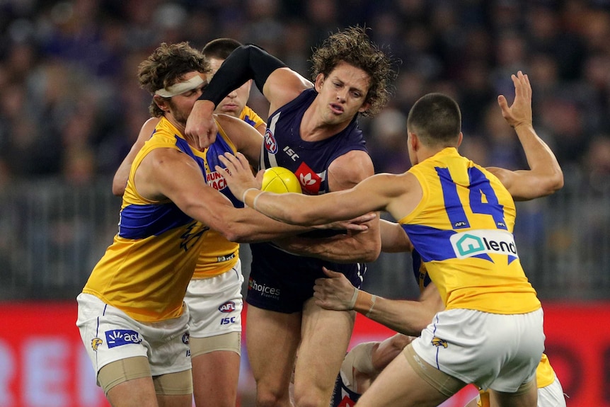 Fremantle Dockers midfielder Nat Fyfe is gang tackled by four West Coast Eagles players as he tries to handpass the ball.