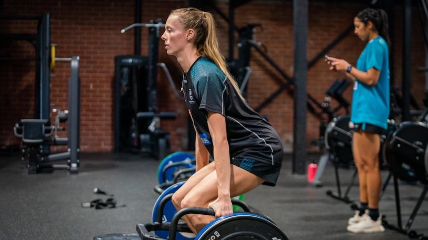 blonde aflw player lighting weights in a gym