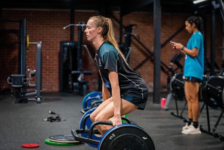 blonde aflw player lighting weights in a gym
