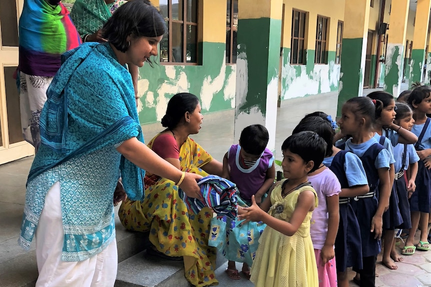 Children lining up to receive a brightly coloured dress from their teacher.