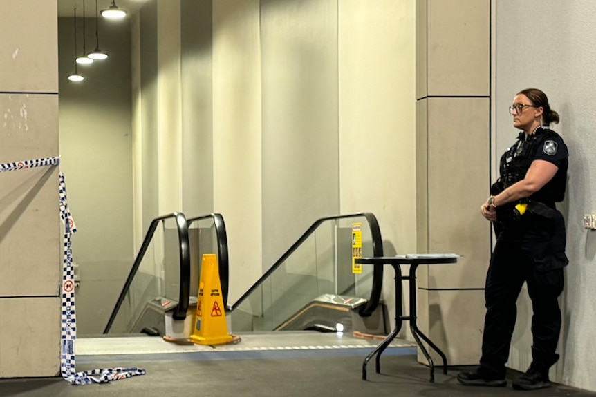 A police officer stands by an escalator with blue and white police tap around it.