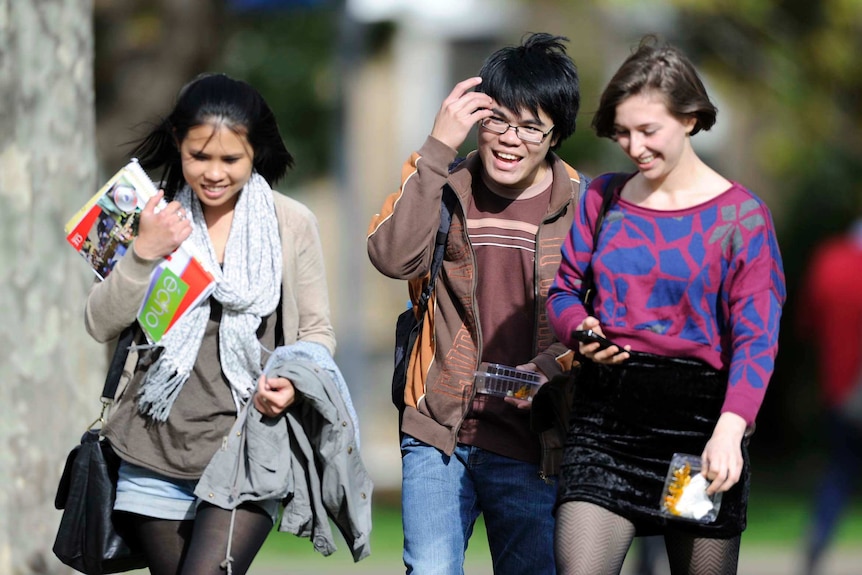 Three young university students smiling and chatting with books in their arms.