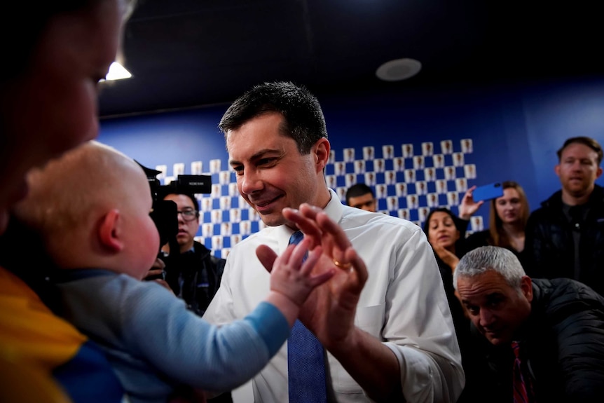 Pete Buttigieg greeting a baby in a crowded campaign event
