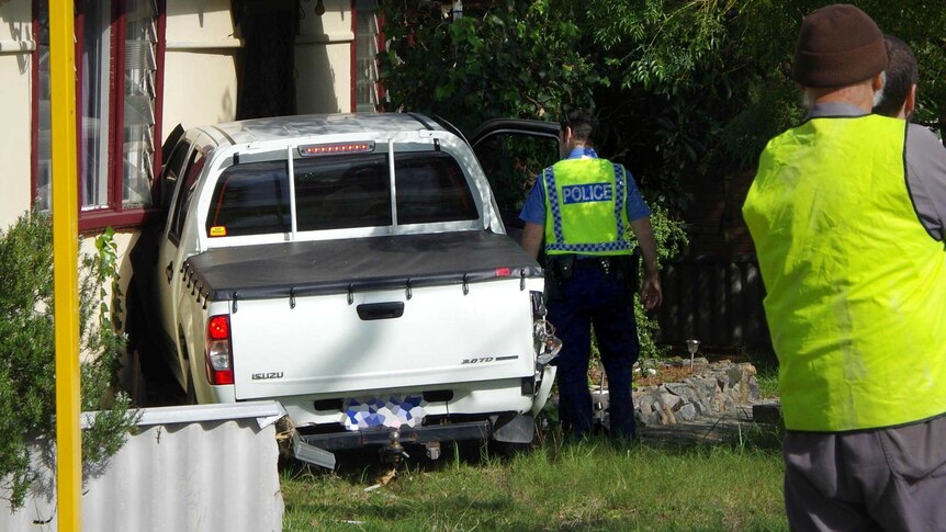 A police officer inspects a car that crashed into a house in the Perth suburb of Gosnells.