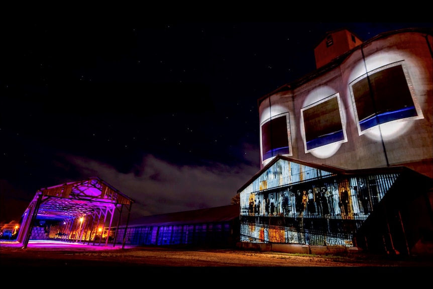 Images of water filling up in a tank projected onto grain silos at night