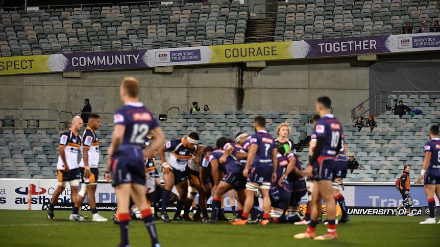 A rugby scrum takes place on the field in front of the stand, showing the sparse crowd.