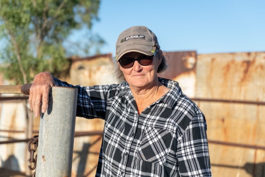 Woman wearing check shirt and baseball hat standing in a horse paddock and smiling