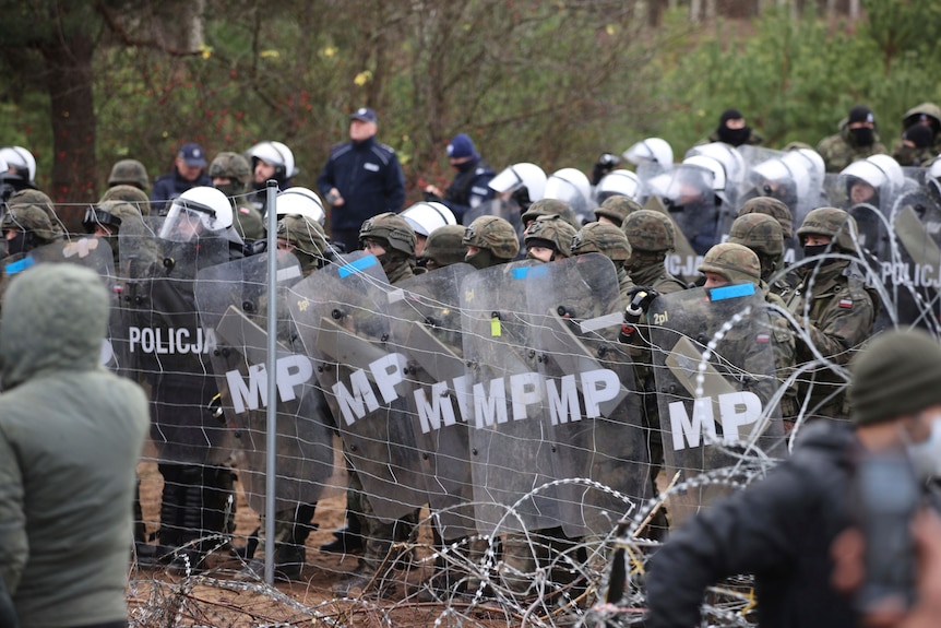 Polish police and military stand next to barbed wire fence on border. 