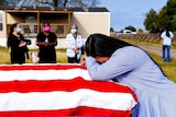 A woman bent over a coffin draped with the US flag