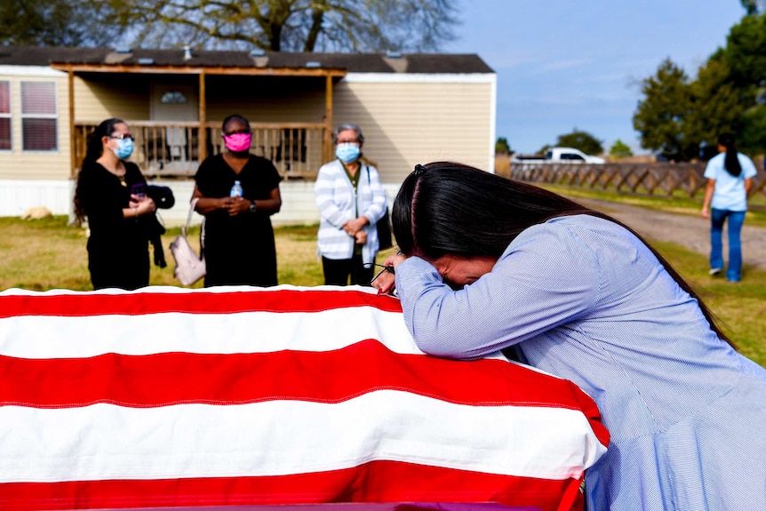 A woman bent over a coffin draped with the US flag