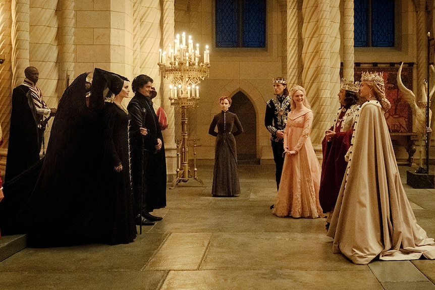 Angelina Jolie and Sam Riley dressed in black stand and face Elle Fanning and Michelle Pfeiffer in large medieval hall.