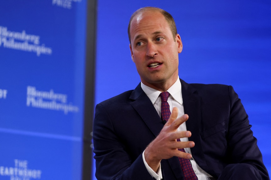 Prince William wears a suit and sits in front of a blue background.