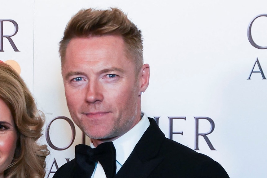 A close up of Ronan Keating smiling at an awards ceremony red carpet