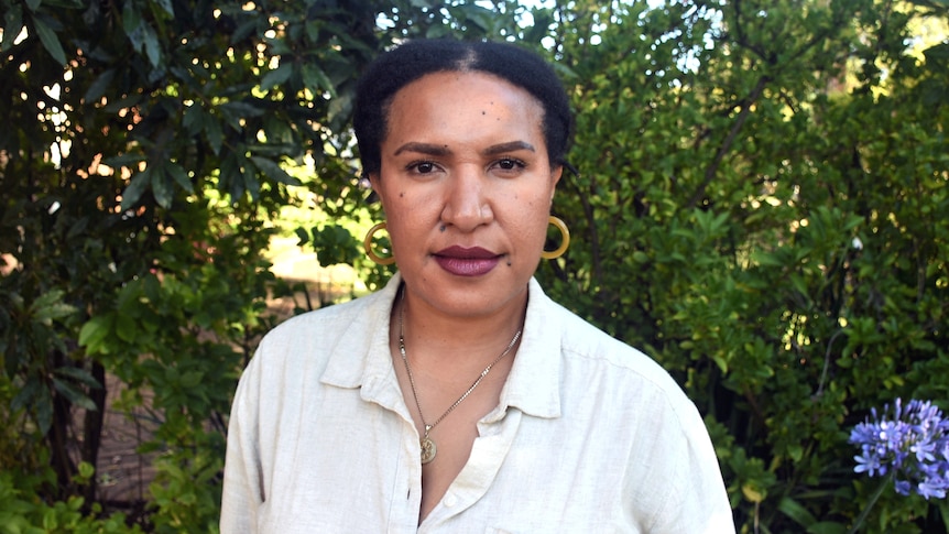 A portrait of Patti LUpari standing in front of a bush.