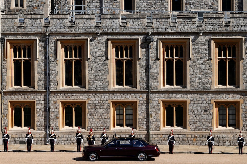 From a wide angle, you view the medieval windows of Windsor Castle with a purple Bentley in the foreground.