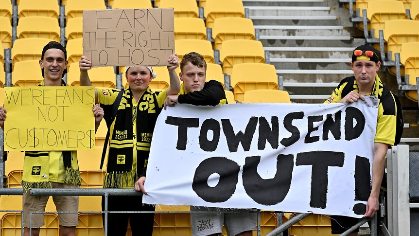 Four Wellington Phoenix fans hold signs protesting about the A-Leagues grand final decision.