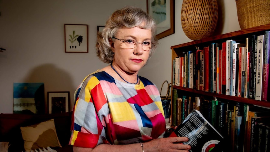 A woman with glasses near a bookcase.