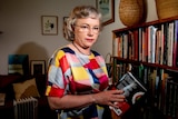 A woman with glasses near a bookcase.