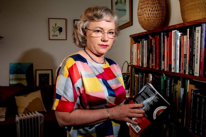 A woman with glasses near a bookcase.