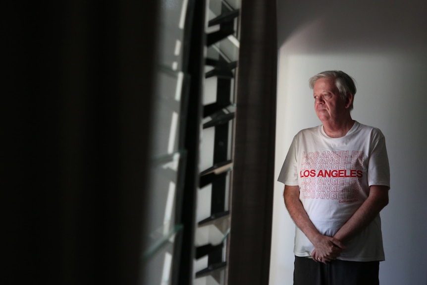 Man with hands together looking out of louvers