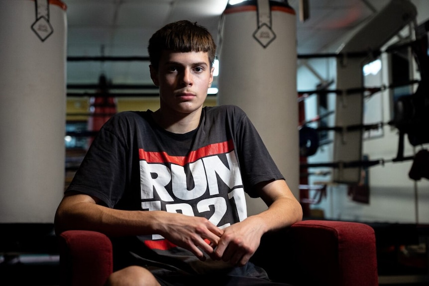 Teenager sits in chair outside boxing ring with hands together 