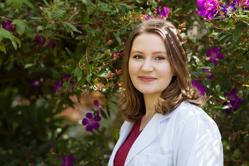 A woman wearing a Western Sydney University lab coat stands under a tree