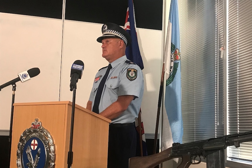 Acting Superintendent Cameron Lindsay speaks to media at the Lismore Police Station with a rifle in the foreground