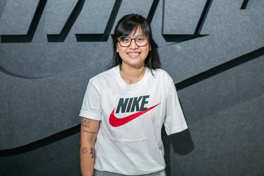 A woman with one arm stands in front of a Nike sign.