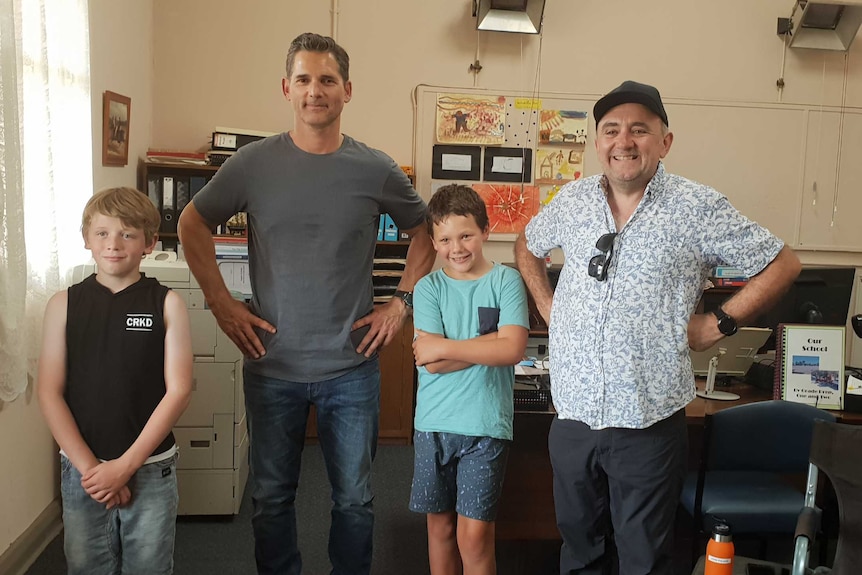 A dark-haired man and a shorter man with a cap stand beside two young boys