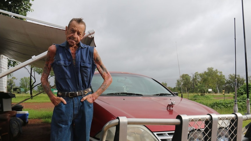 A man poses with hands in pockets next to a red ute with a large bullbar.