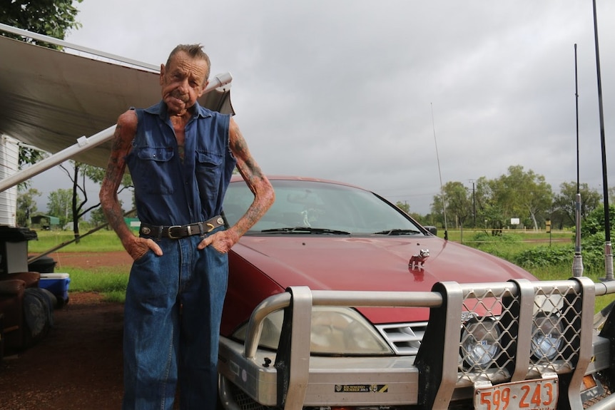 A man poses with hands in pockets next to a red ute with a large bullbar.