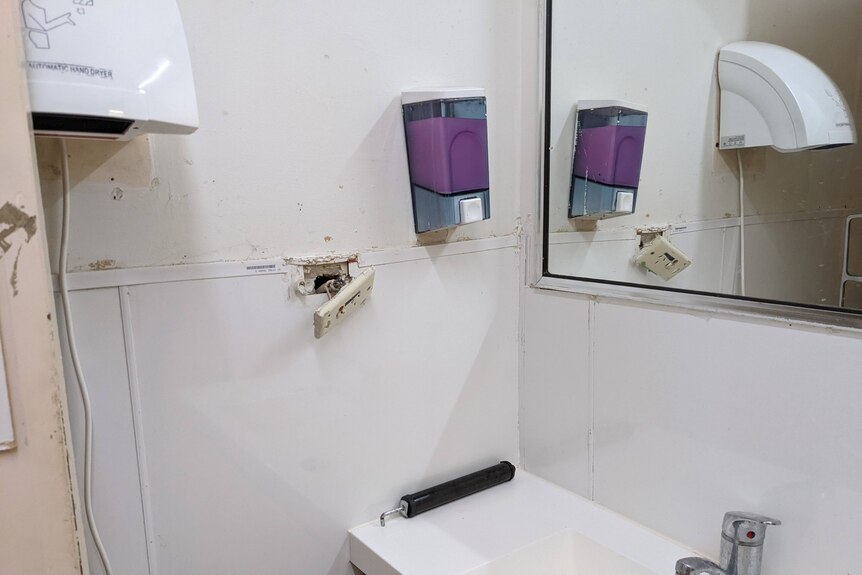 A bathroom with marks on the walls and a power point torn from the wall.