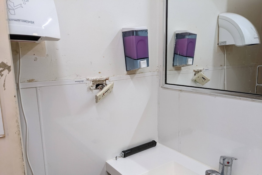 A bathroom with marks on the walls and a power point torn from the wall.