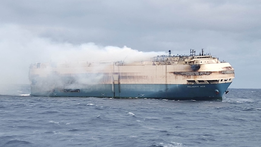 Smoke billows off a huge white and ship in the middle of the ocean
