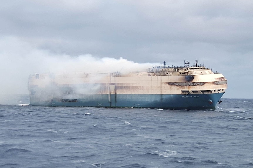 Smoke billows off a huge white and ship in the middle of the ocean