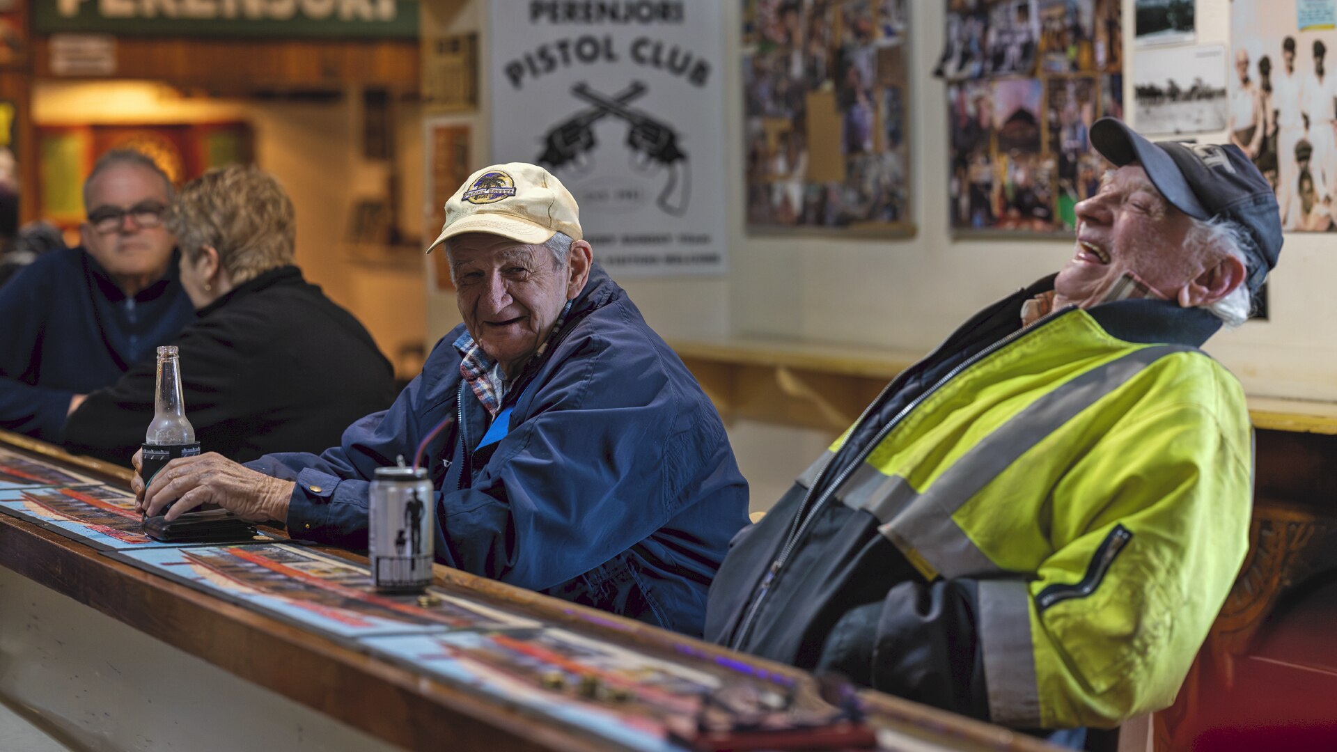 Two old men sit at the bar and laugh while drinking beer