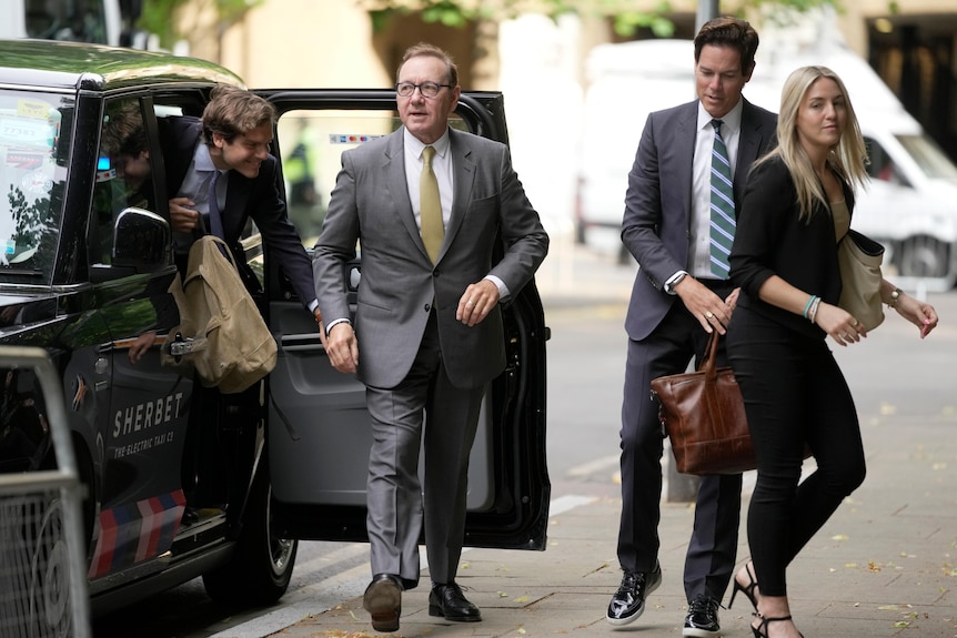 Kevin Spacey is pictured wearing a suit as he gets out of a black cab. With him are two men and a woman, also in suits.