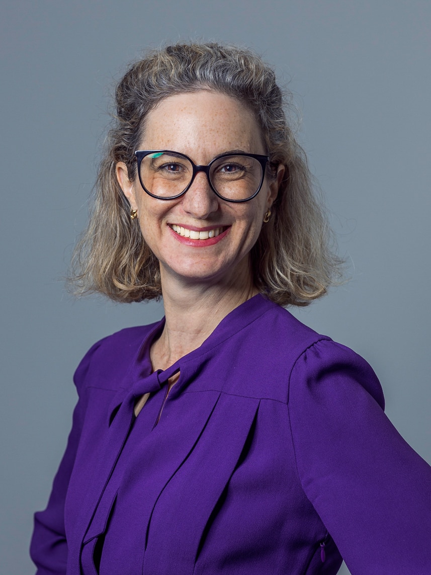 Woman with glasses and purple shirt smiles at the camera