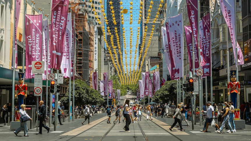 People walking across Bourke Street Mall in Melbourne with Christmas decorations above.
