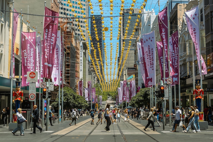 People walking across Bourke Street Mall in Melbourne with Christmas decorations above.
