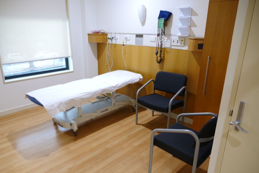 An empty hospital bed and two chairs in a hospital room.