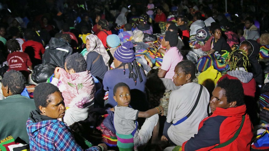 Backs of densely packed group of West Papuan civilians sitting on the ground.