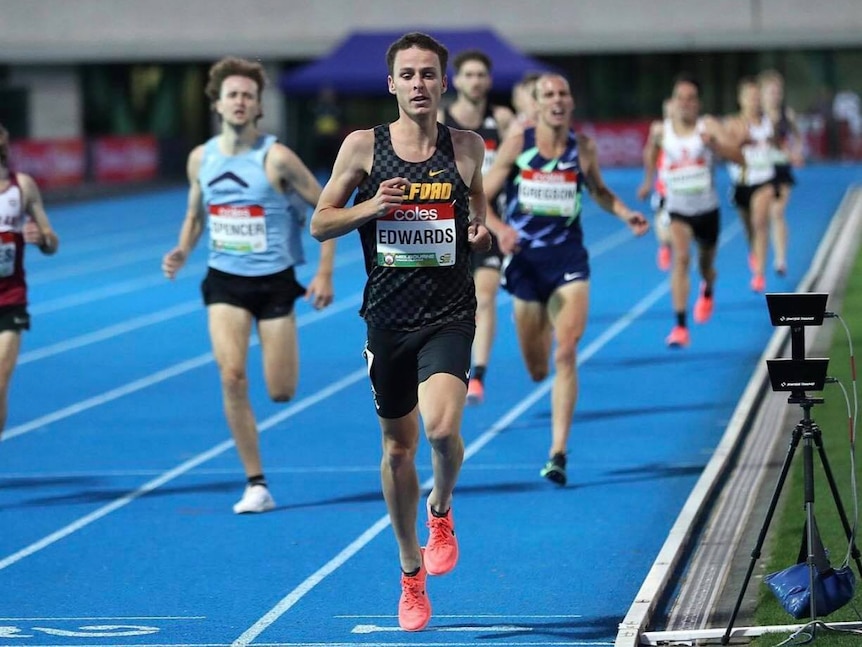 A runner runs towards the camera while other runners finish behind him on a running track