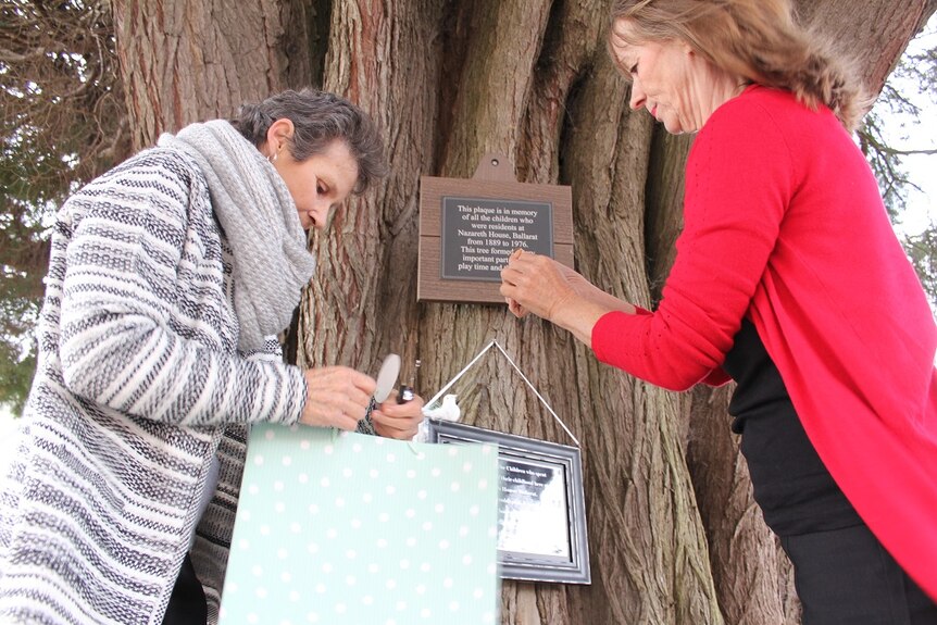 Gabrielle Short and Wendy Dykof nail their home-made plaque to a tree.