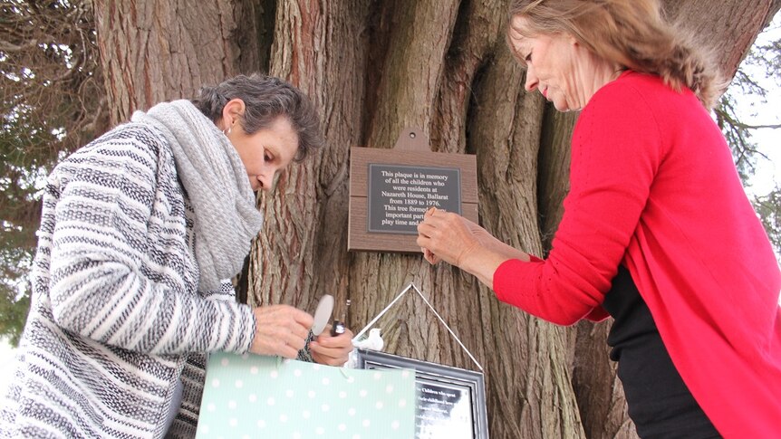 Gabrielle Short and Wendy Dykof nail their home-made plaque to a tree.