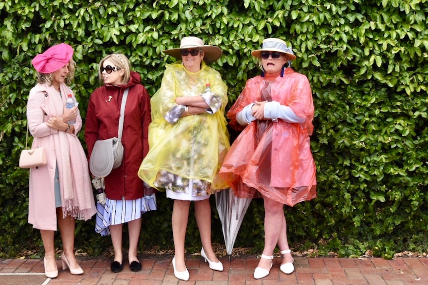 Four women stand in coats and ponchos.