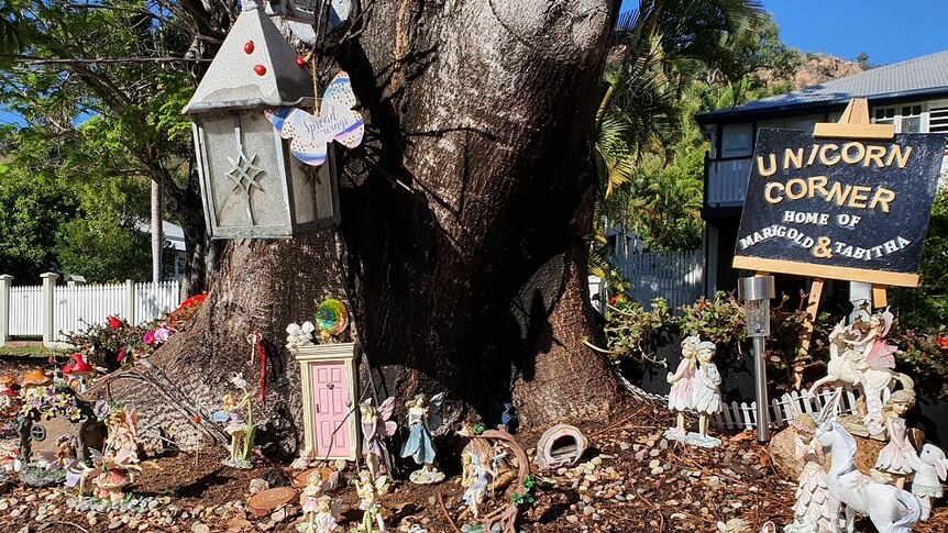 A fairy garden complete with little pink door at the base of a big tree and little figurines of fairies, unicorns, and flowers