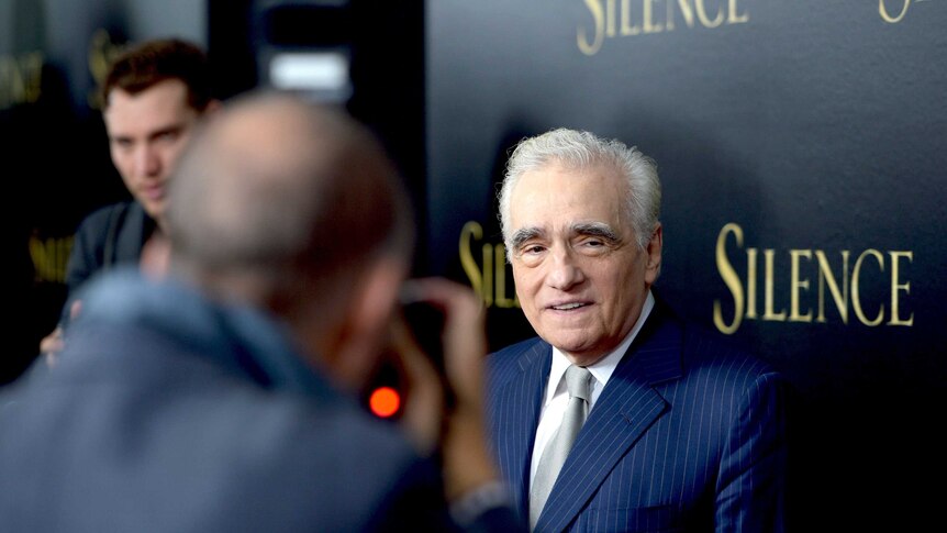 Director Martin Scorsese stands in front of a sign for his film Silence as photographers surround him